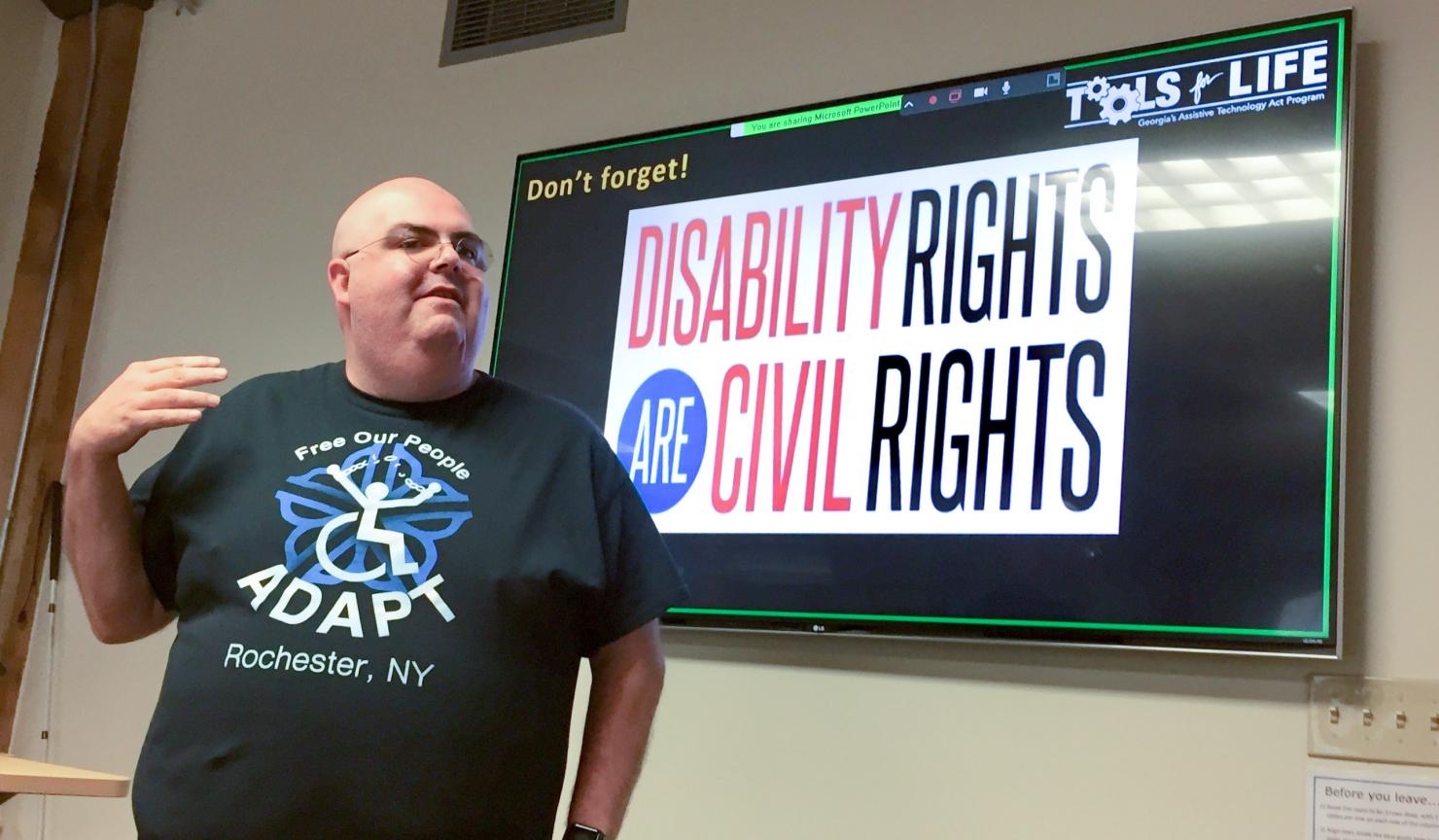 A presenter stands in front of a screen with the words 'Disability Rights are Civil Rights'