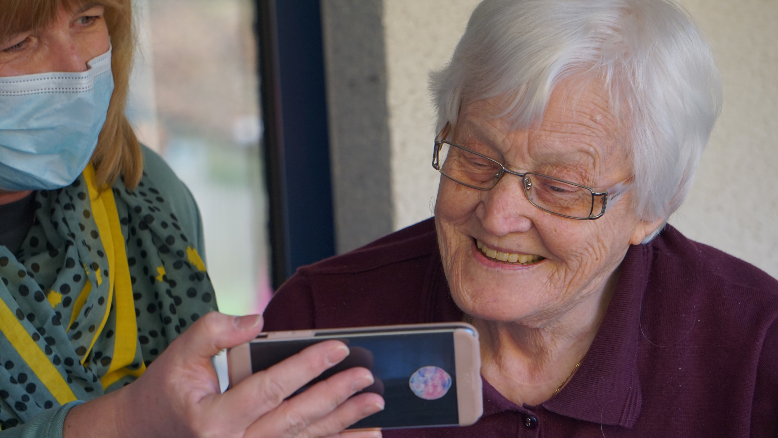 woman showing an elderly woman an app on a cell phone.