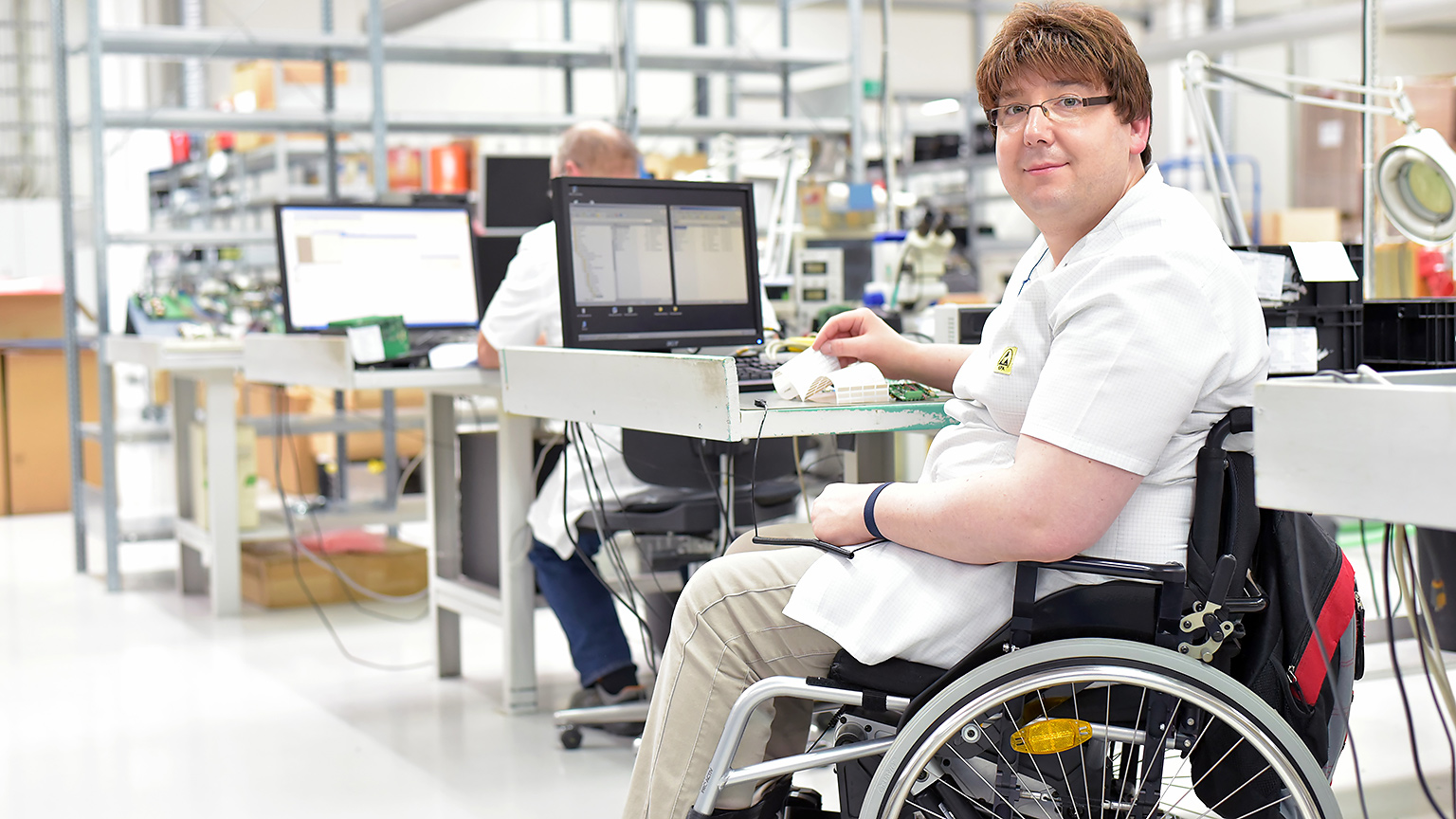A man who uses a wheelchair works at a computer in a technology sector office.